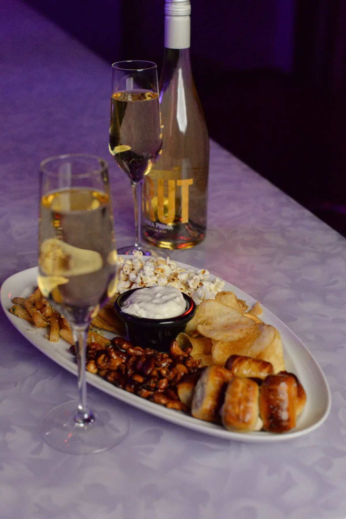 Lola’s snack board with pretzel bites, chips, popcorn, nuts, dip, and Brut
